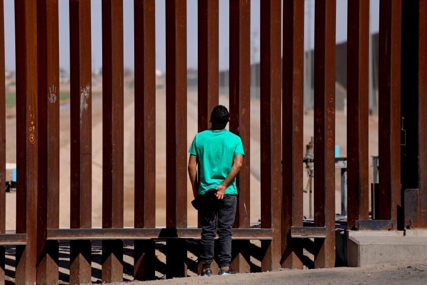 SAN LUIS COLORADO, SONORA - MAY 11: An immigrant admires the border wall while waiting to turn himselft over to U.S Border Patrol agents along the U.S.-Mexico border on Thursday, May 11, 2023 in San Luis Colorado, Sonora. Title 42, a pandemic-era policy that allowed border agents to quickly turn back migrants, expires this week. Under a new rule, the U.S. on Thursday will begin denying asylum to migrants who show up at the U.S.-Mexico border without first applying online or seeking protection in a country they passed through. (Gary Coronado / Los Angeles Times)