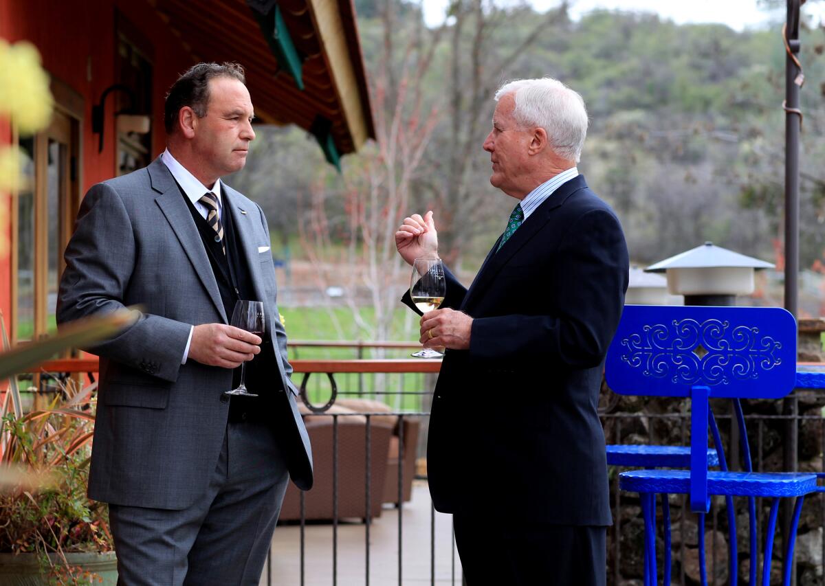 Two men in suits holding wine glasses on a patio