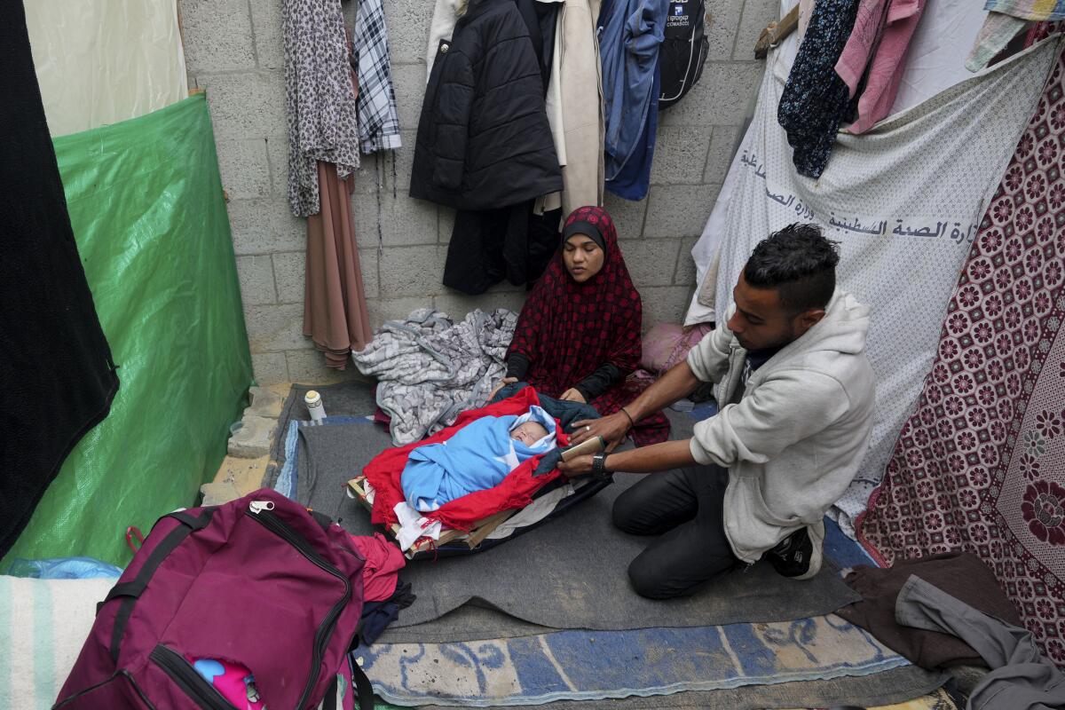 Palestinians displaced by the Israeli bombardment of the Gaza Strip sit around their newborn daughter at their makeshift tent