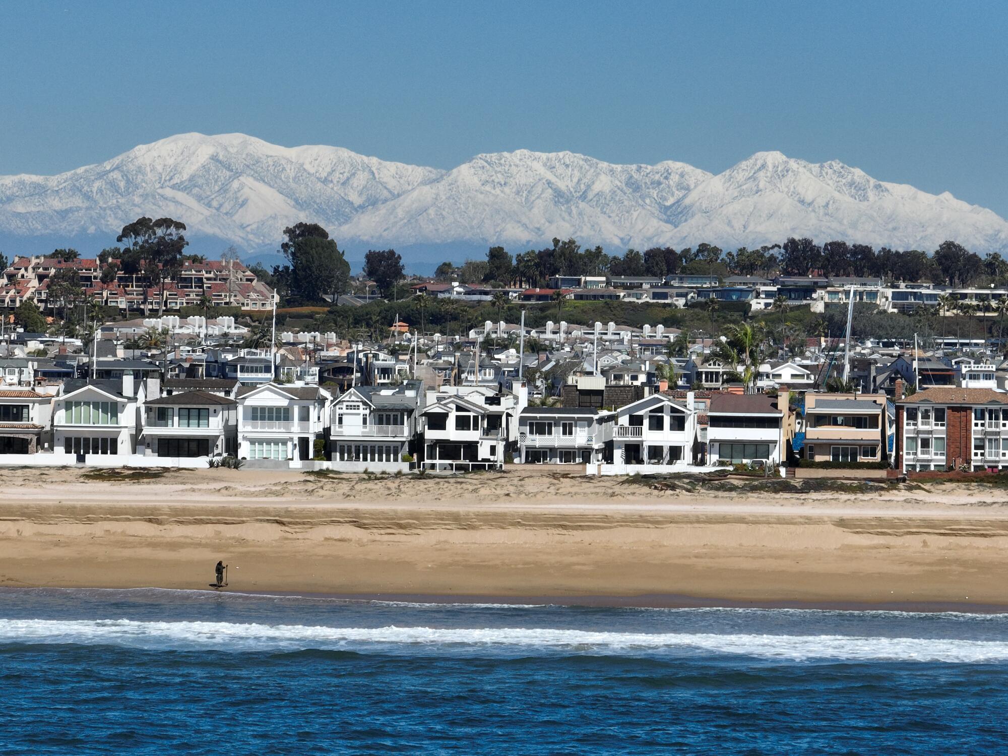 An aerial view of the surf, a beach comber and a panoramic view of snow-capped San Gabriel Mountains.