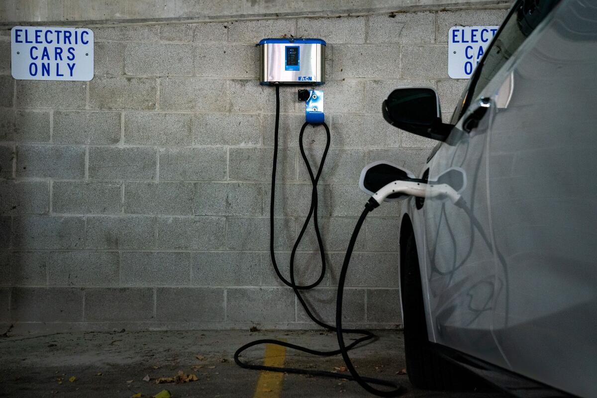 An electric vehicle charges at a charging station in a parking garage next to signs that say "electric cars only"