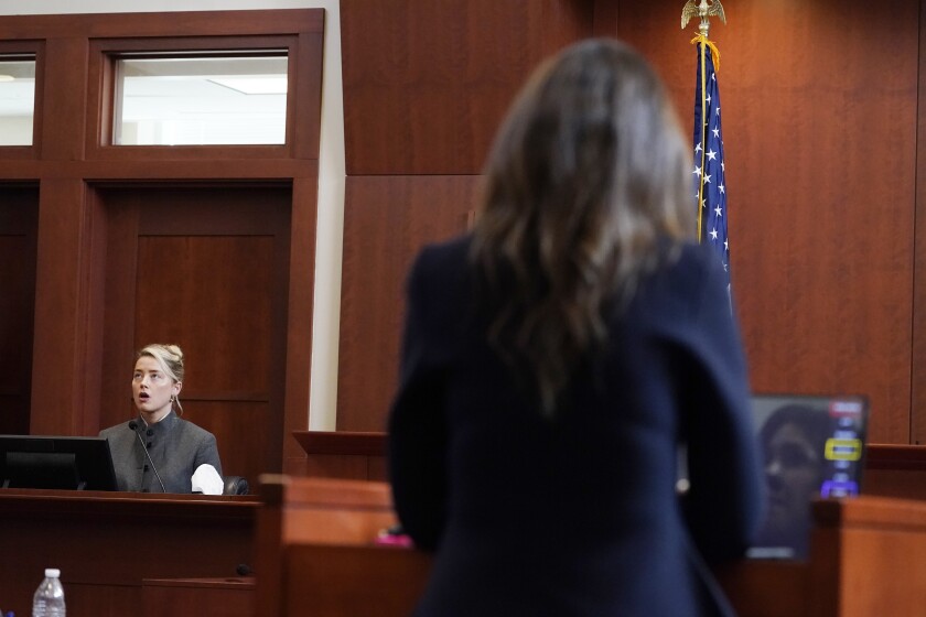 A woman sitting on the witness stand is cross-examined by a female attorney who is seen from behind