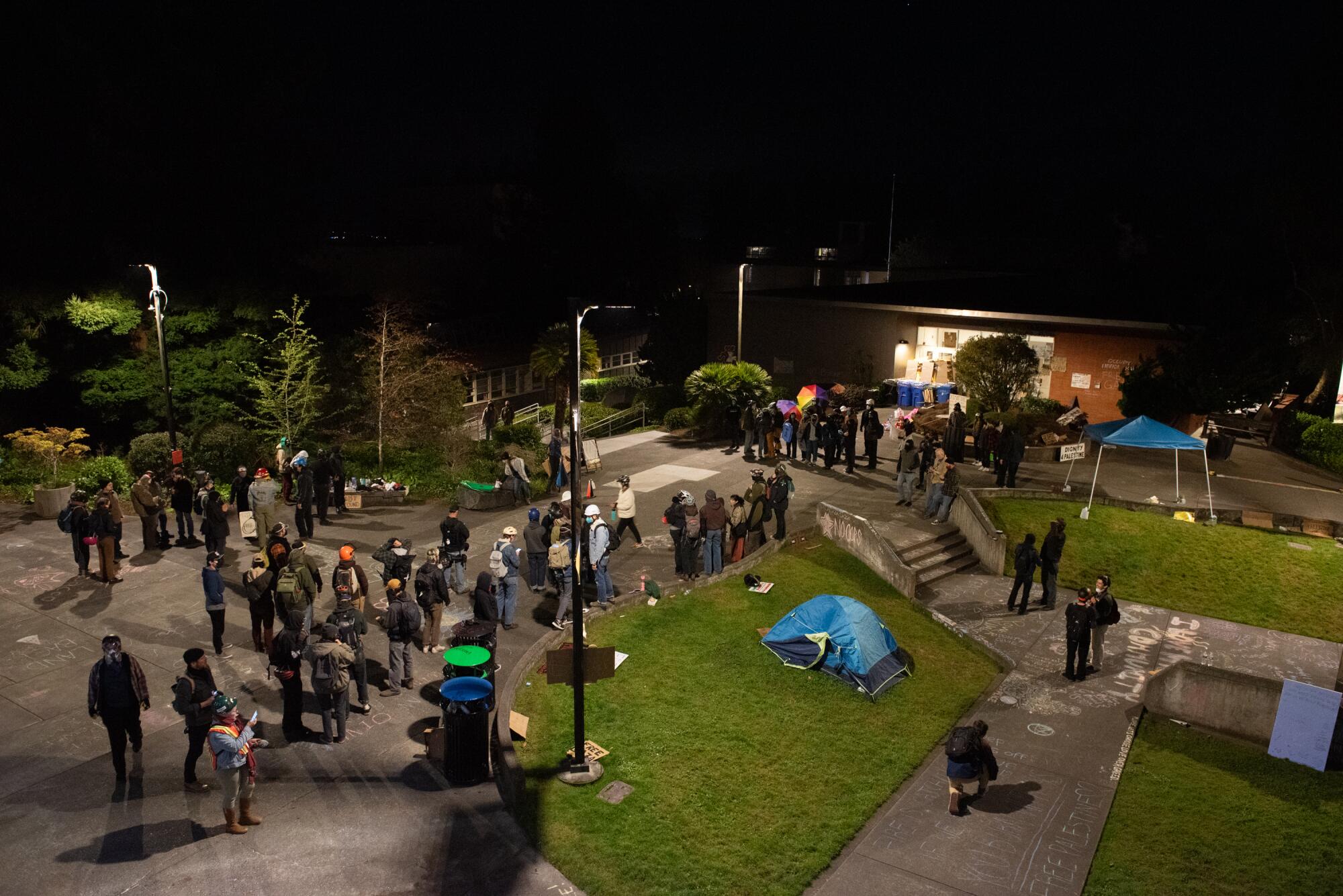 Students line a sidewalk near a tent outside a campus building.