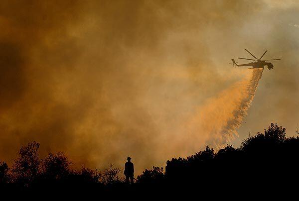 A U.S. Forest Service firefighter monitors the Station fire as a helicopter makes a water drop on a ridge along Angeles Crest Highway in La Ca?ada Flintridge.