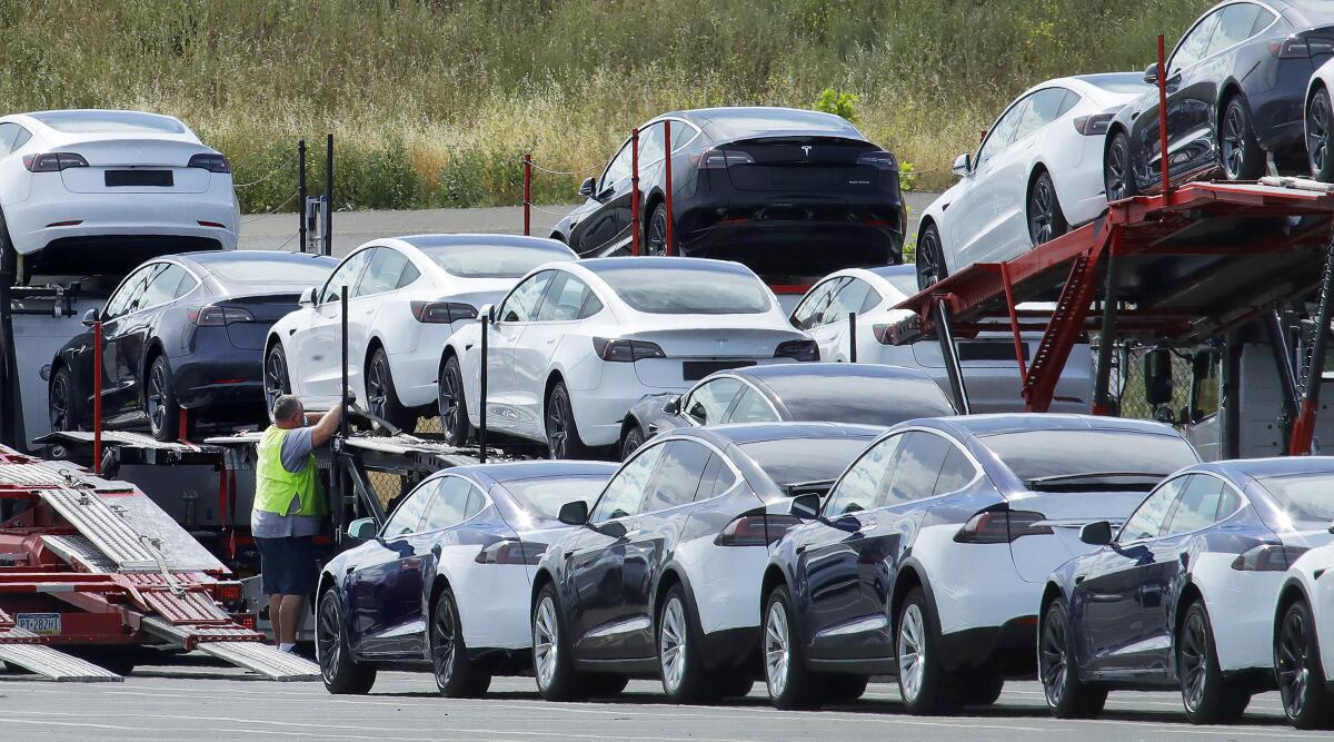 More than a dozen black and white Teslas are loaded onto car carriers. 
