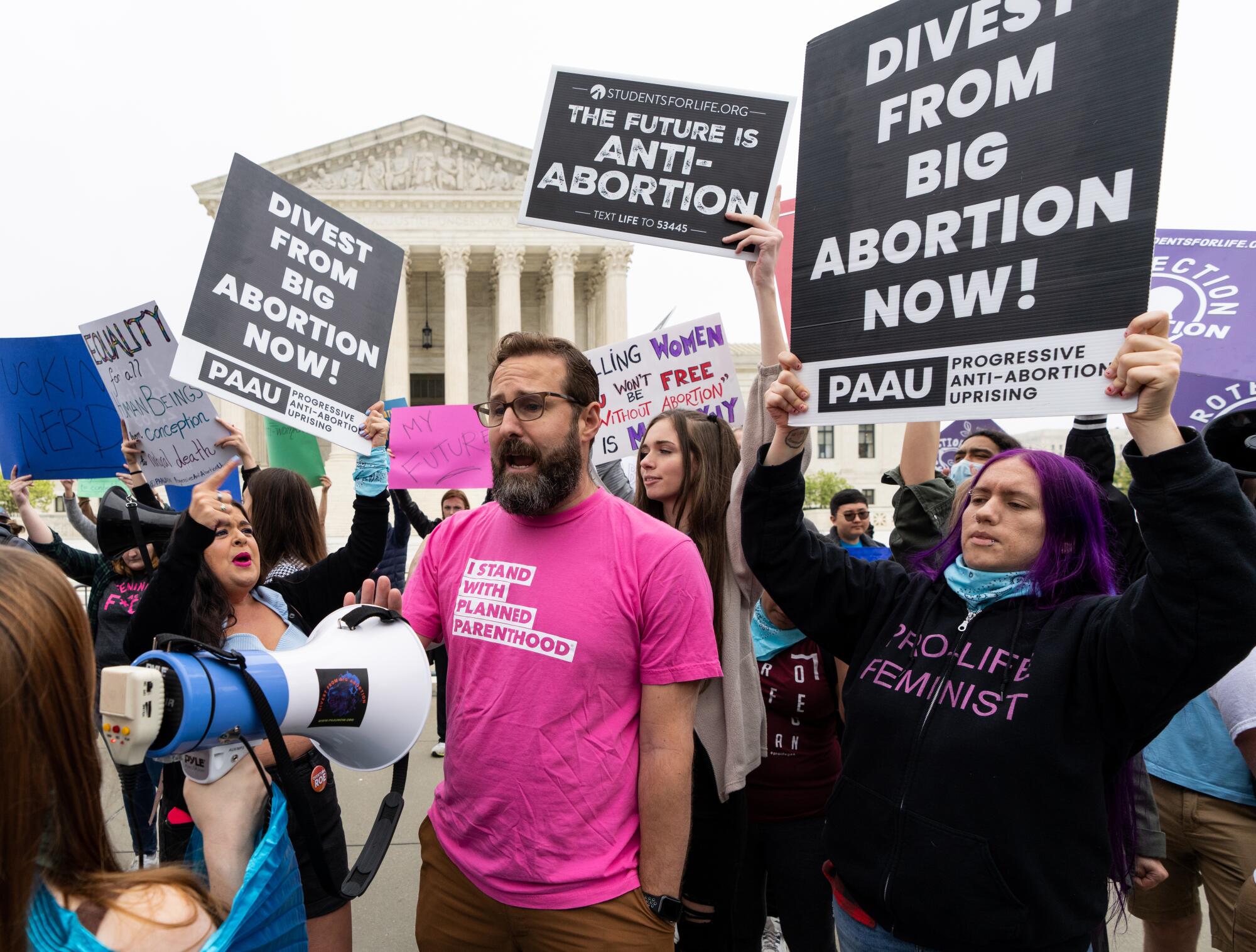 Antiabortion activists with "Divest from Big Abortion now!" signs surround a man in a Planned Parenthood shirt.
