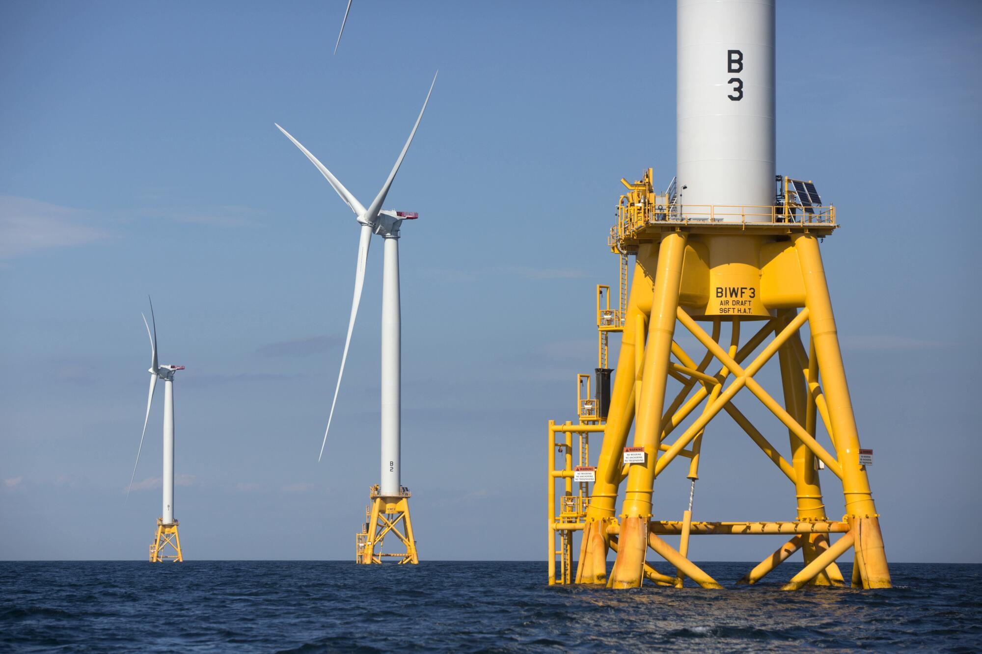 Three offshore wind turbines rise from a calm sea.