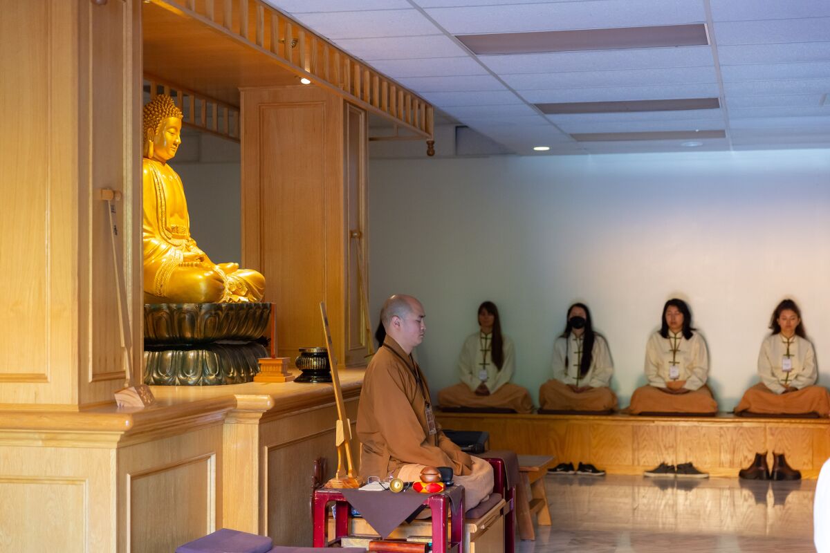 A monk leads a meditation in front of a Buddha statue