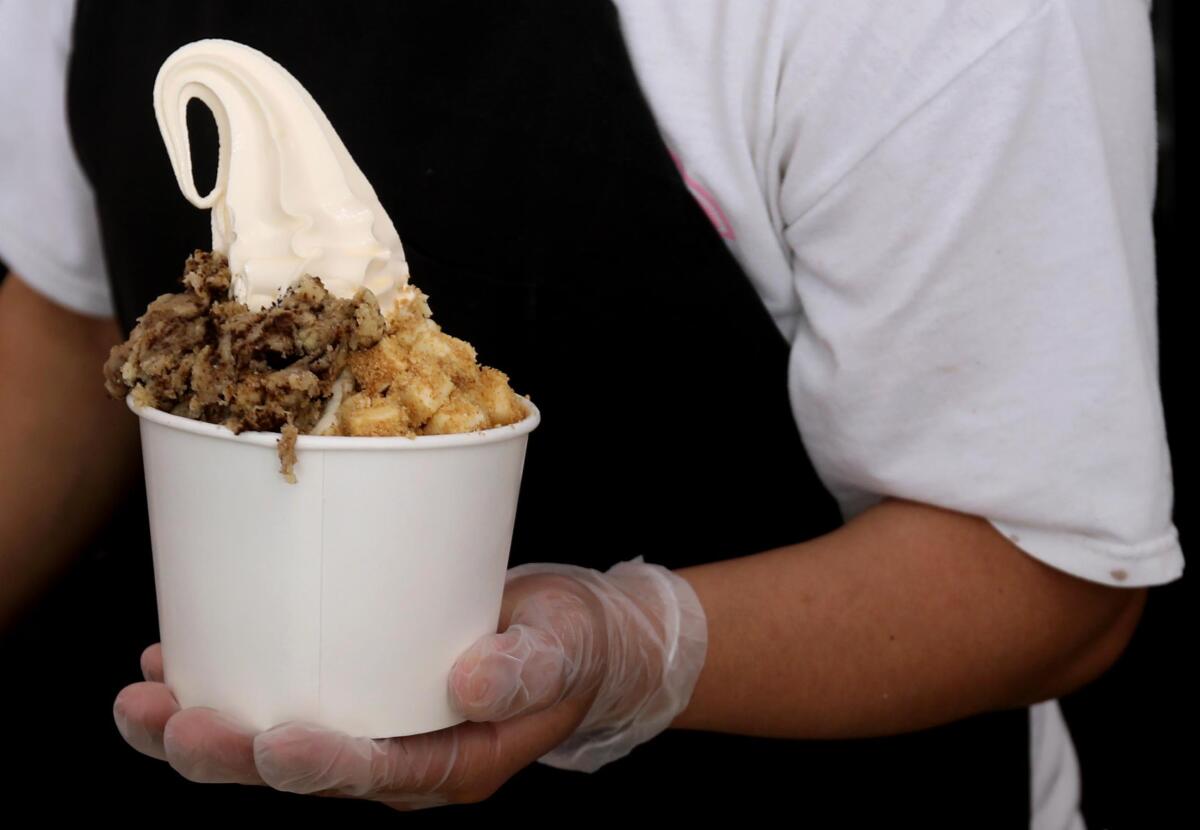 A gloved hand holds a cup of vanilla frozen yogurt assorted toppings