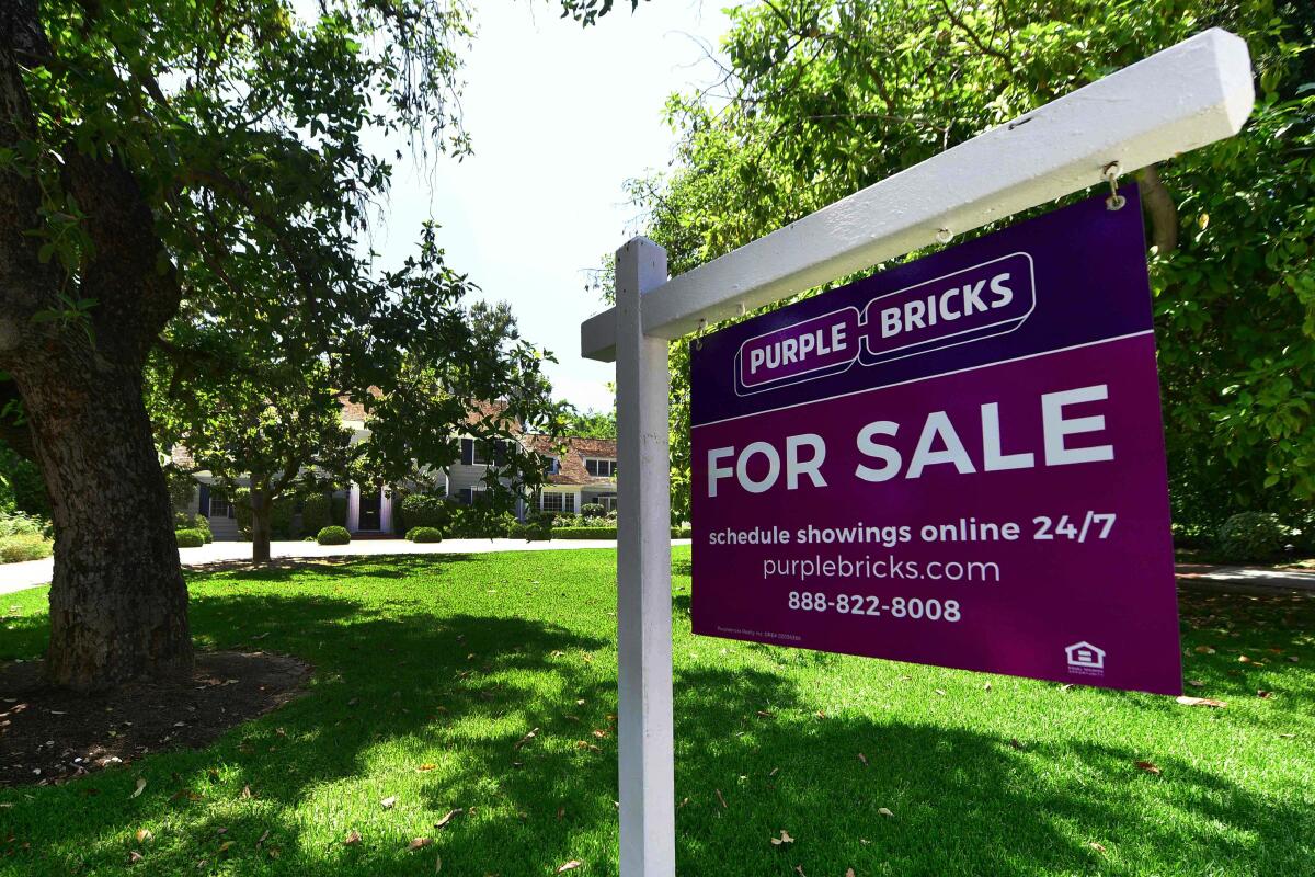 A Purple Bricks "for sale" sign outside a home with a large lawn and big trees