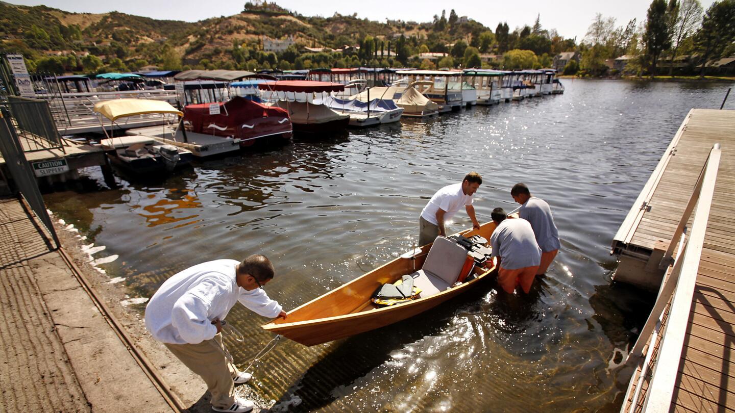 A teacher helps students launch a solar-powered boat in the lake.