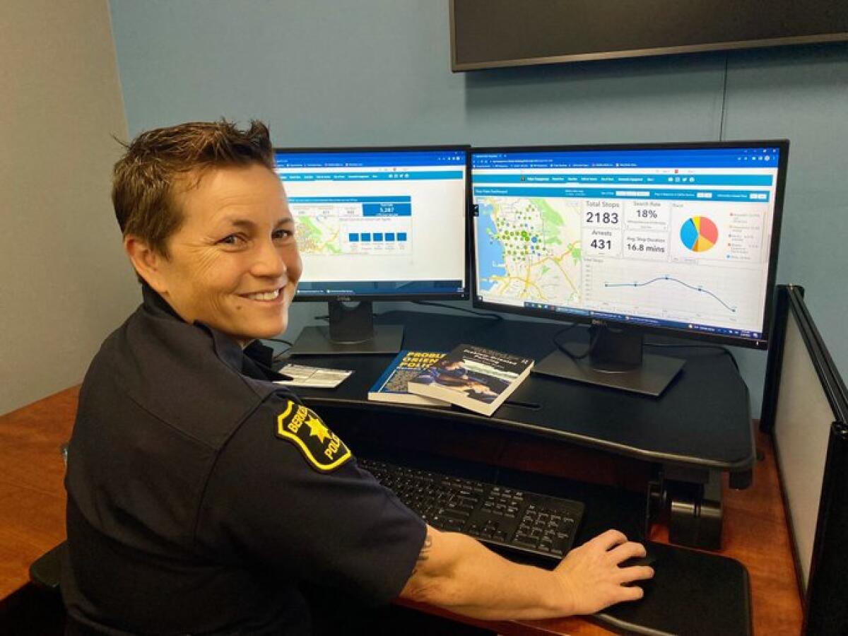 A woman in a police uniform looks back, smiling, while sitting at a computer.