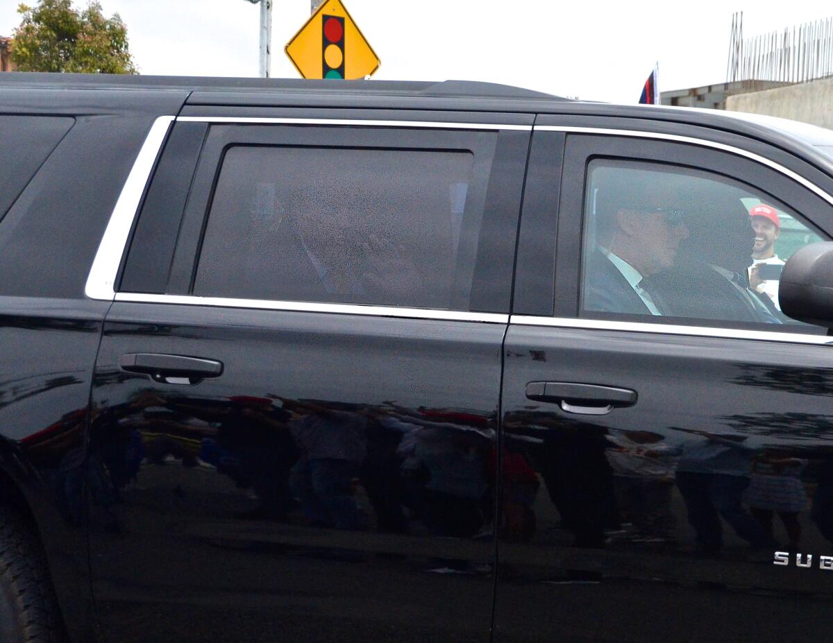 Former President Trump waves from behind thick glass in a Suburban as it passes along Bayside Drive.