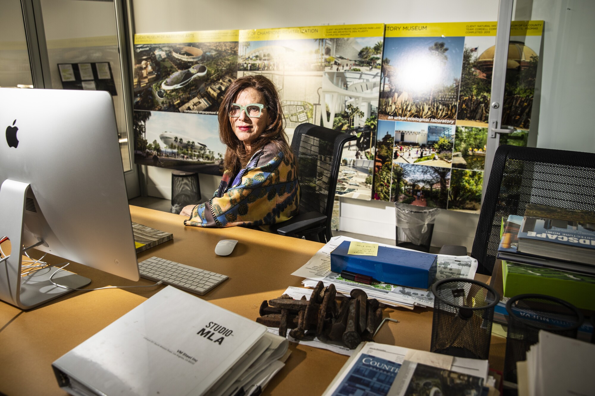 Mia Lehrer at her desk in an office lined with landscape design schematics.
