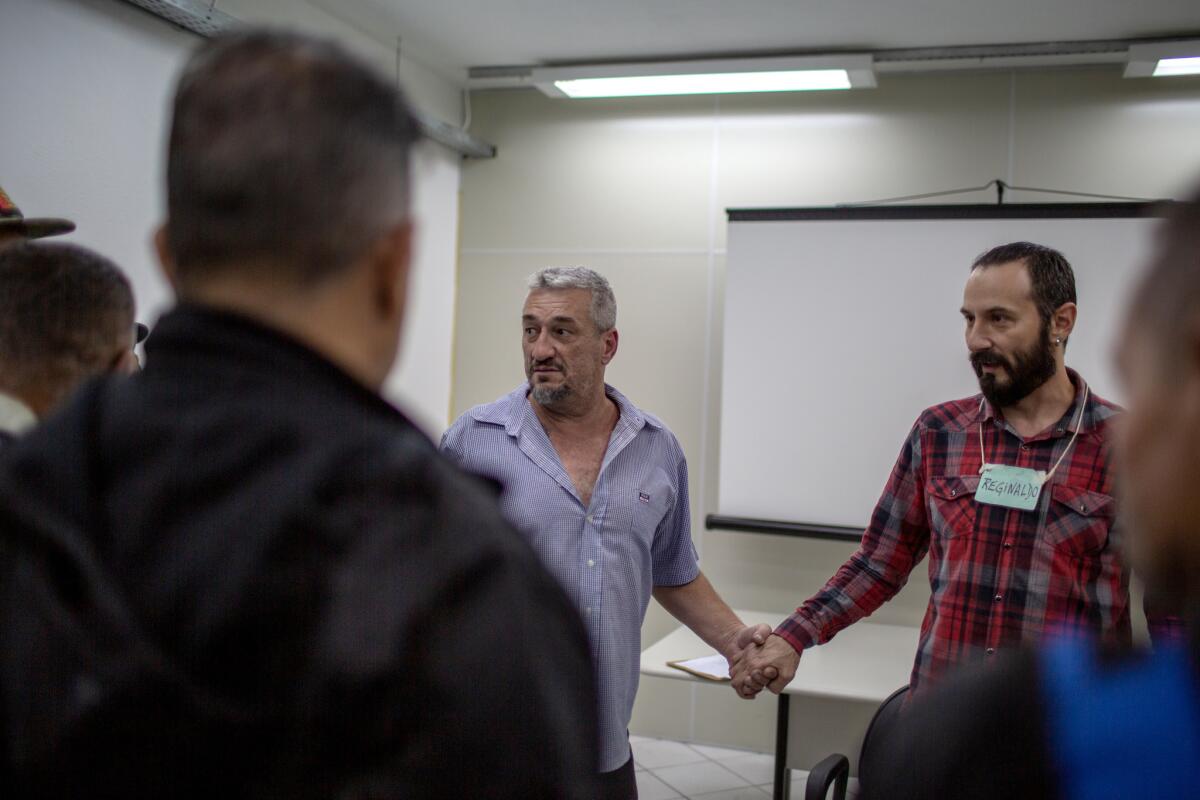 Ricardo Serafine, left, holds the hand of group facilitator Reginaldo Bombini as they and other participants of a therapy group for men serving alternative sentences for domestic violence convictions wrap up their session with final words of support.