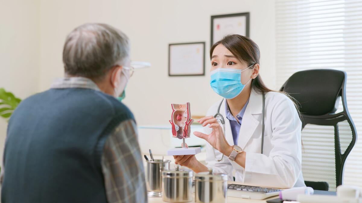 A doctor showing an elder patient a rectal model of various health issues such as hemorrhoids, anal fissures.