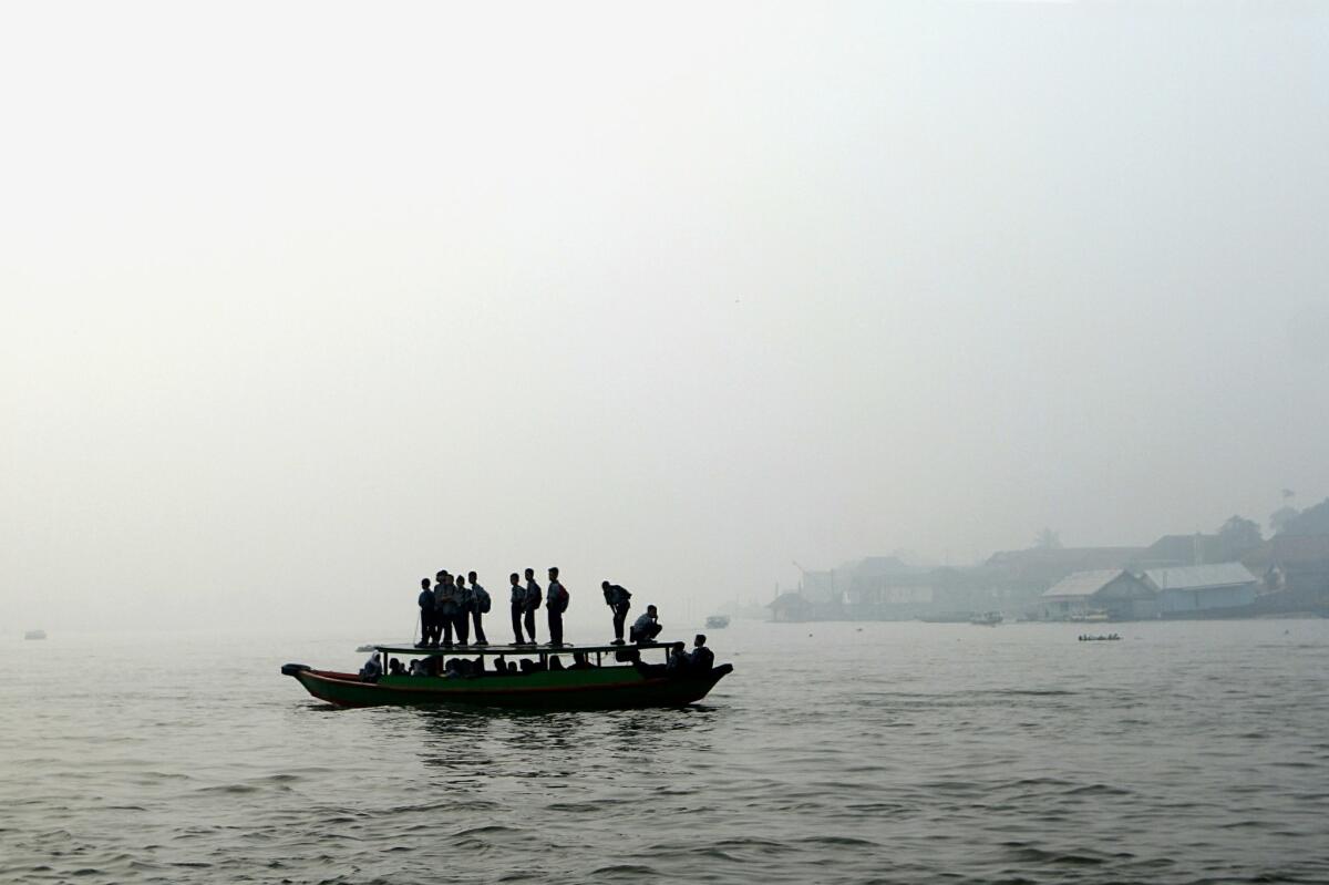 Indonesian students cross a river by boat under a blanket of haze from forest fires on Sumatra island.