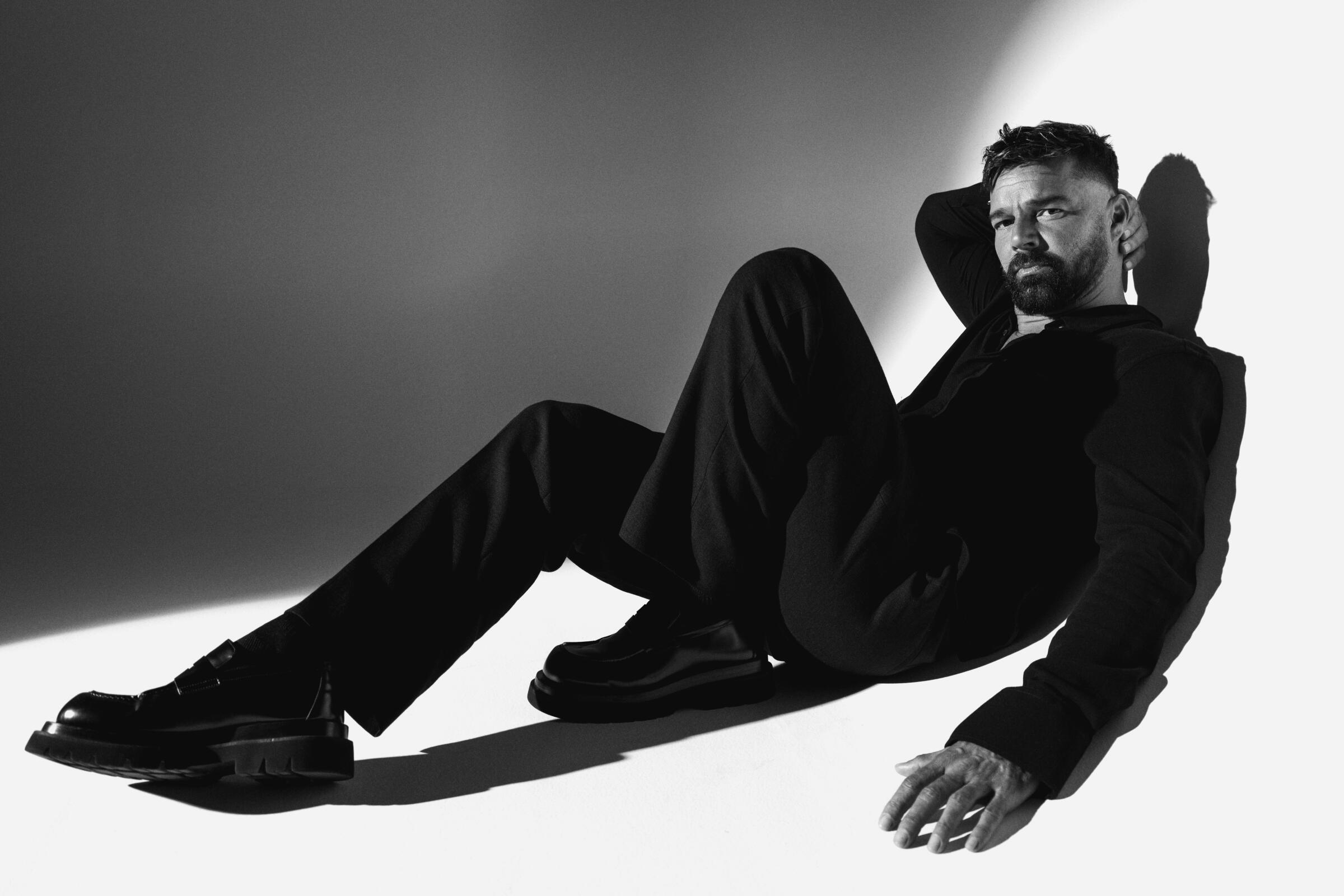 Ricky Martin leans back against a stark backdrop for a black-and-white portrait.