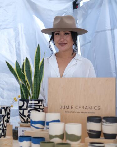 A vendor wearing a hat stands behind her ceramic wares at In Todo Craft Fair.