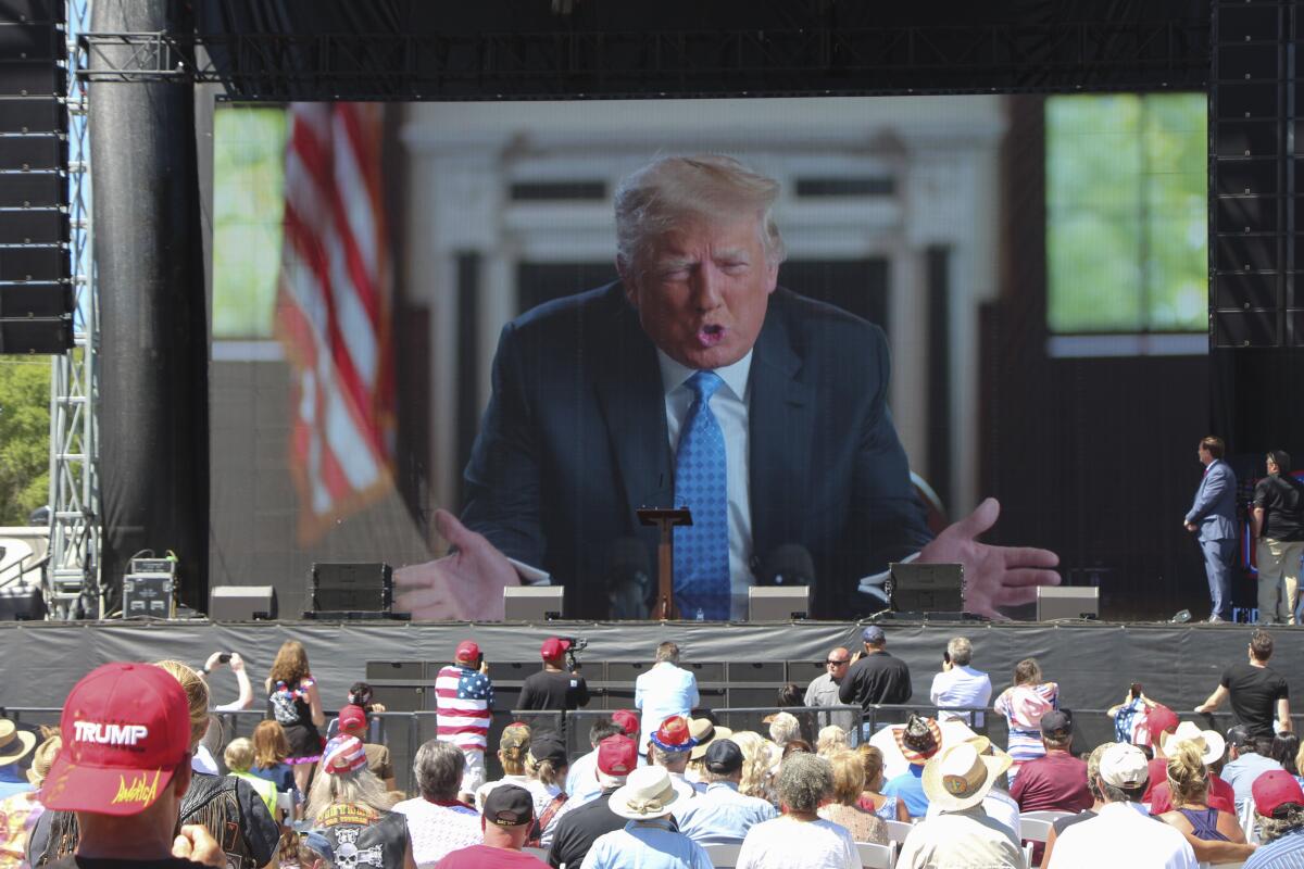 Former President speaking on a giant screen to a crowd.