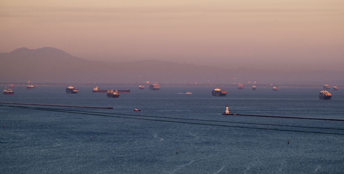 The sunset illuminates dozens of container ships in the ocean off the coast