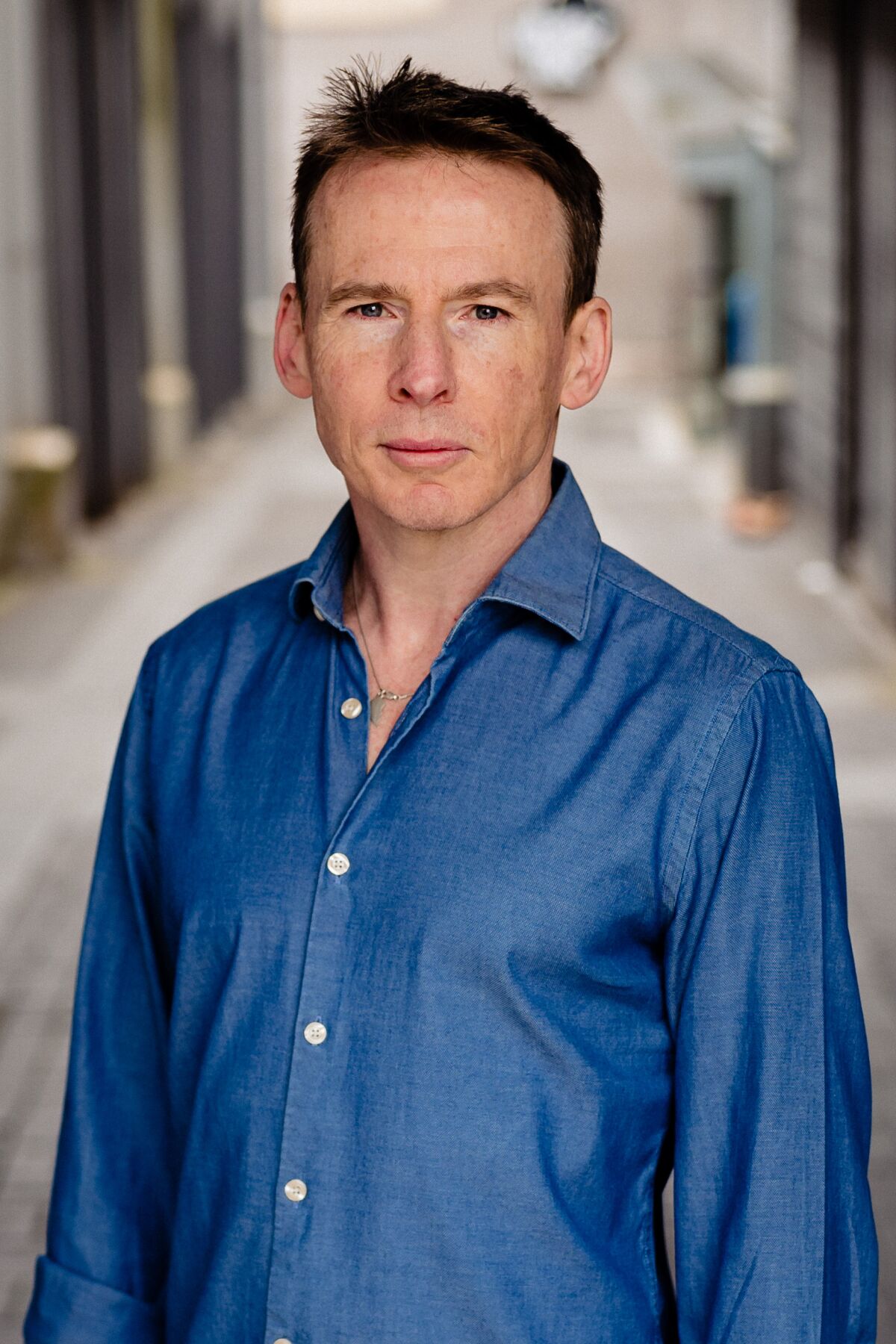 Rory Carroll, an author, in a crisp blue shirt standing in an alley.