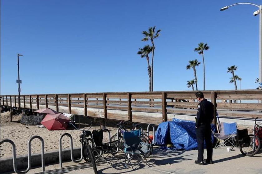 Tony Yim, a homeless liaison officer with the Newport Beach Police Department, speaks with homeless people staying at the Balboa Pier on Feb. 6.