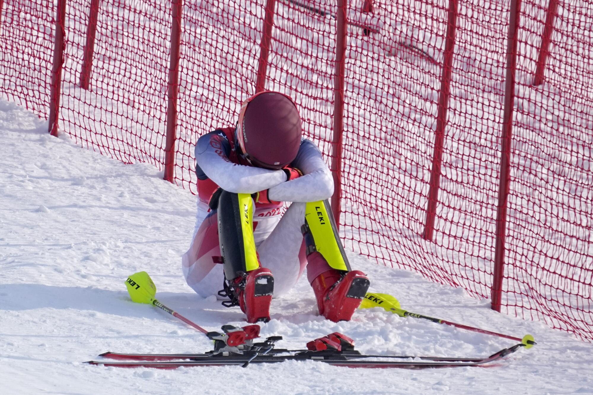 U.S. skier Mikaela Shiffrin sits in the snow with her head buried in her arms, her skis and poles on the ground next to her