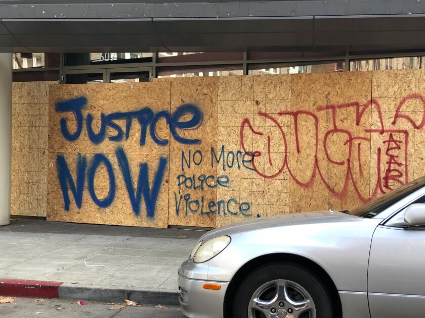 Graffiti on plywood that says Justice Now and No More Police Violence