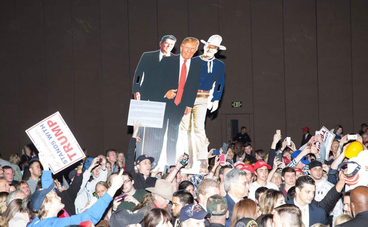 Attendees hold up a cardboard printout of presidential candidate Donald Trump standing in front of former president Ronald Reagan and actor John Wayne at a Trump campaign rally in Fort Worth, Texas on Feb. 26.