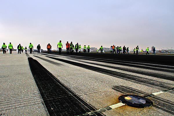 Los Angeles International Airport personnel wearing safety vests or bright-colored T-shirts take part in the first runway walk, picking up debris to clear Runway 24R on the north side of the airport.