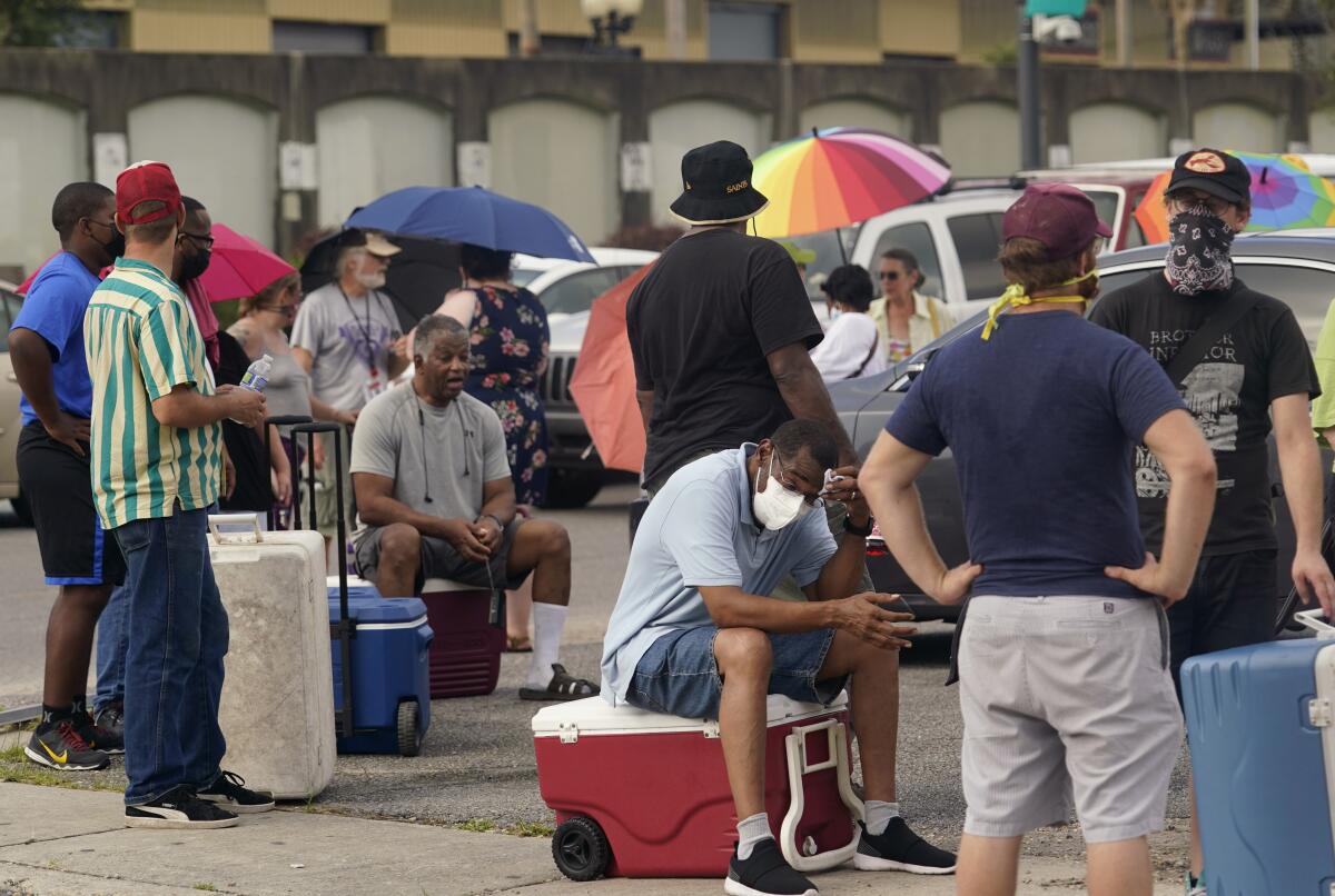 Louisiana residents sit on coolers or stand, some with umbrellas, in the heat
