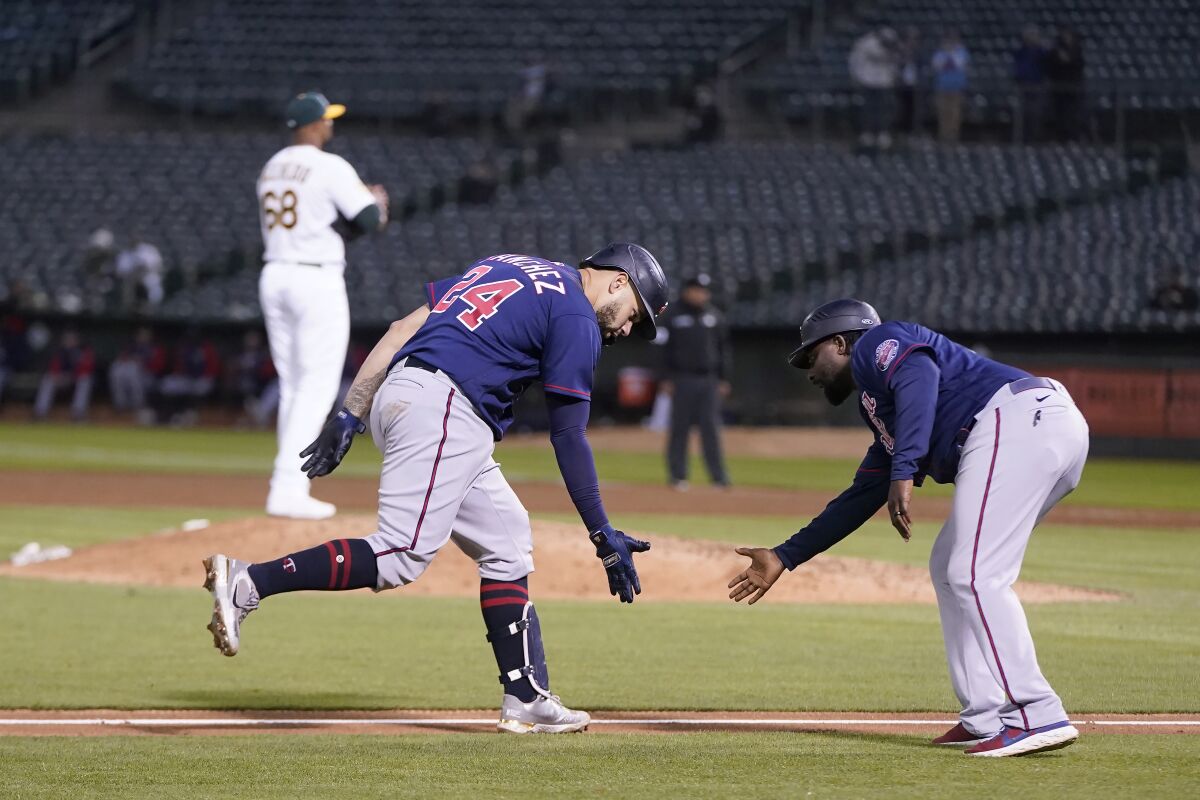 Minnesota Twins' Gary Sanchez, bottom left, is congratulated by third base coach Tommy Watkins after hitting a home run off of Oakland Athletics pitcher Domingo Acevedo, rear, during the sixth inning of a baseball game in Oakland, Calif., Monday, May 16, 2022. (AP Photo/Jeff Chiu)