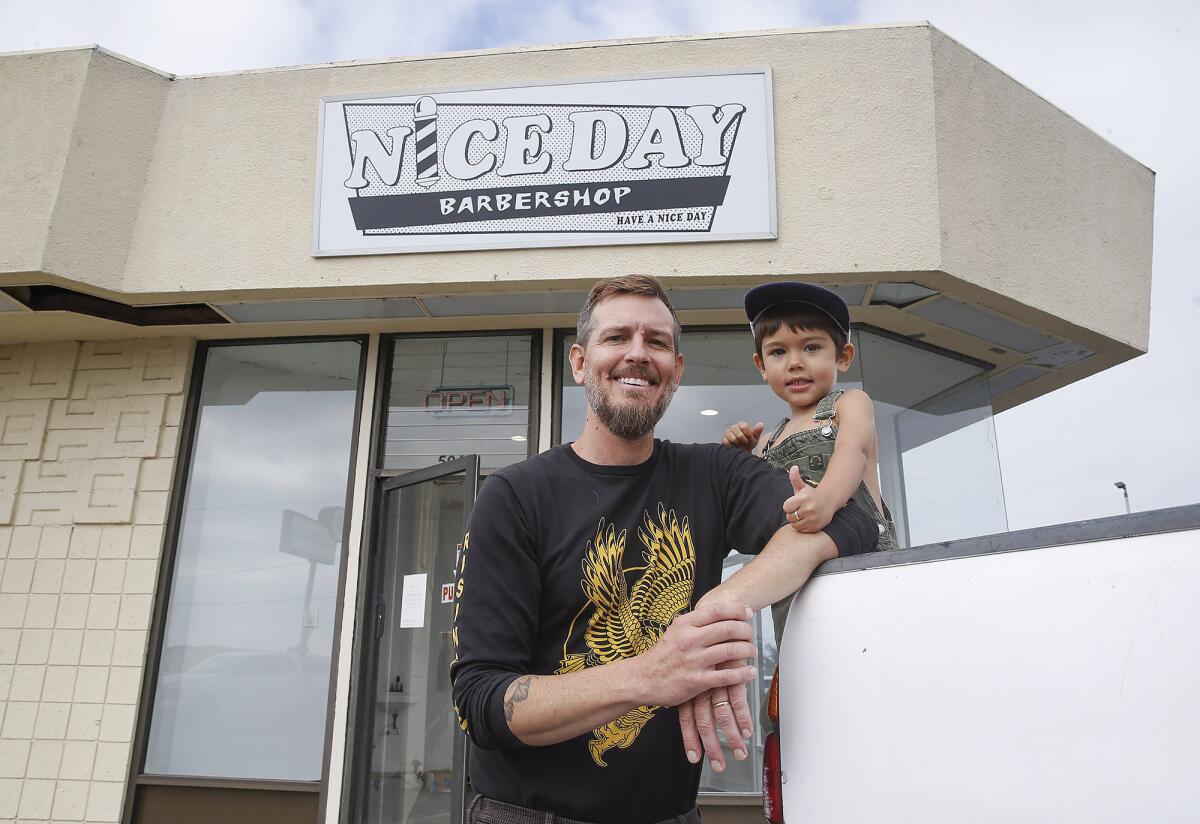 Jake Bushnell with his son Rocky under his new sign for Nice Day Barbershop, a beach-vibe barbershop.