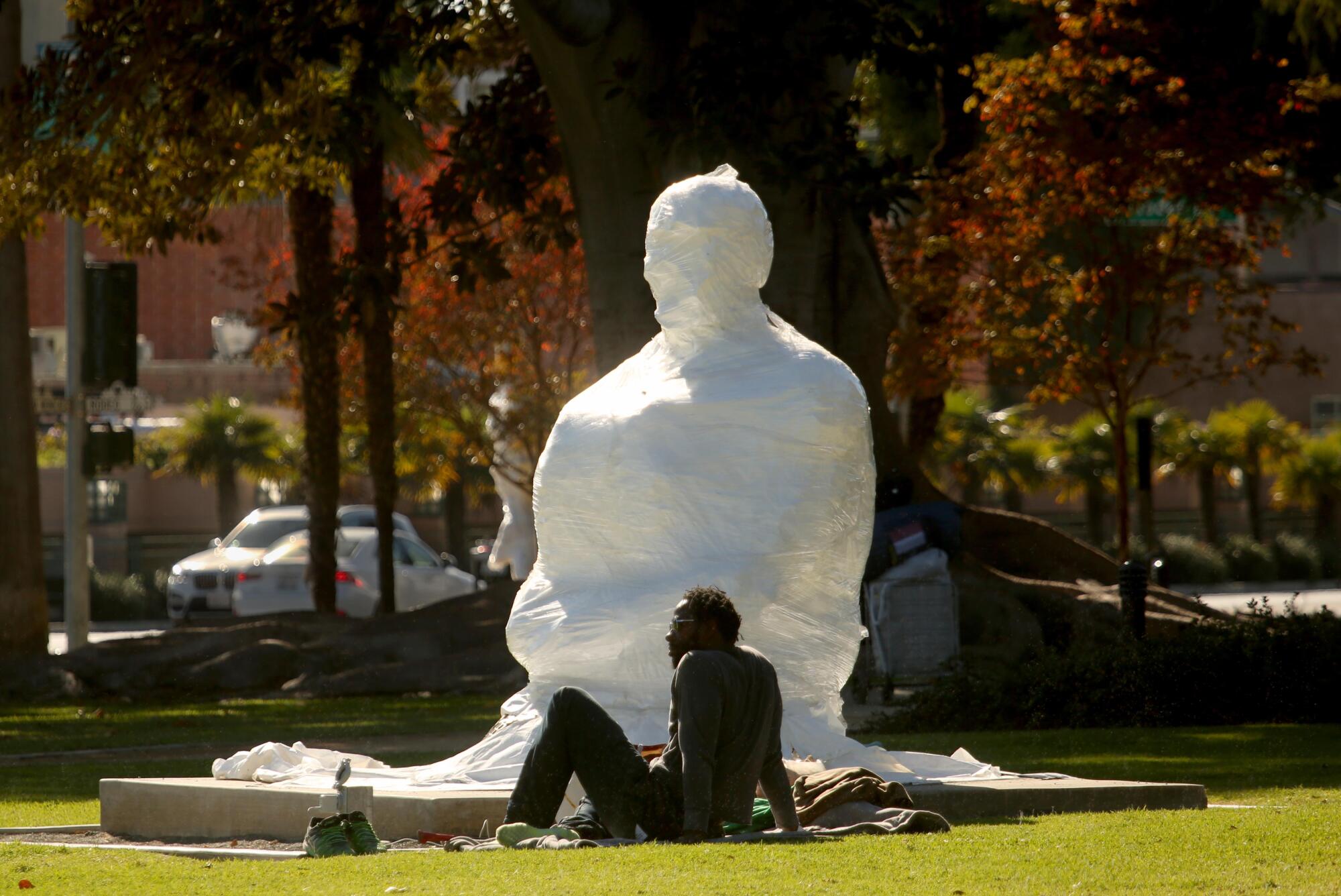A man sits on the grass near a sculpture 