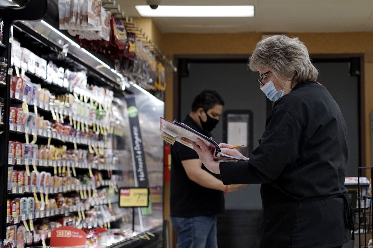 FILE - A grocery store's employee wears mask and gloves to protect against coronavirus, as she checks products at a grocery store in Mount Prospect, Ill., Wednesday, May 13, 2020. The nation’s largest food and retail union is urging more than 60 retail and grocery chains to implement stronger measures to help protect hourly workers amid a surge of virus infections and the new variant omicron. (AP Photo/Nam Y. Huh, File)