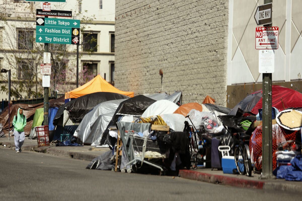 A man walks along a row of tents and enclosures in skid row on March 26.