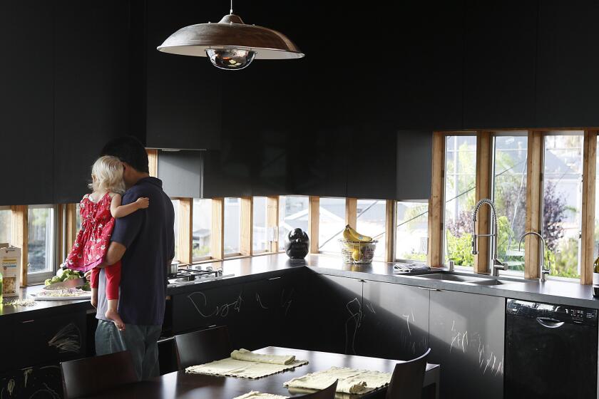 Robert Choeff holds daughter Zara in his Venice kitchen, where the dark cabinets in chalkboard paint leave the emphasis on views and conceal the refrigerator and other appliances. The paint and polished concrete floors make the kitchen feel expansive, even though it's a mere 125 square feet.