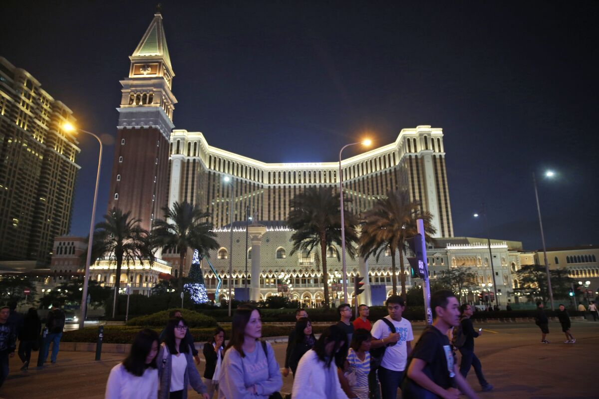 FILE - People walk in front of the Venetian Macao casino resorts in Macao, Nov. 23, 2014. The Asian gambling center of Macao will close all its casinos for a week starting Monday, July 11, and largely restrict people to their homes as it tries to stop a COVID-19 outbreak that has infected more than 1,400 people in the past three weeks. (AP Photo/Kin Cheung, File)