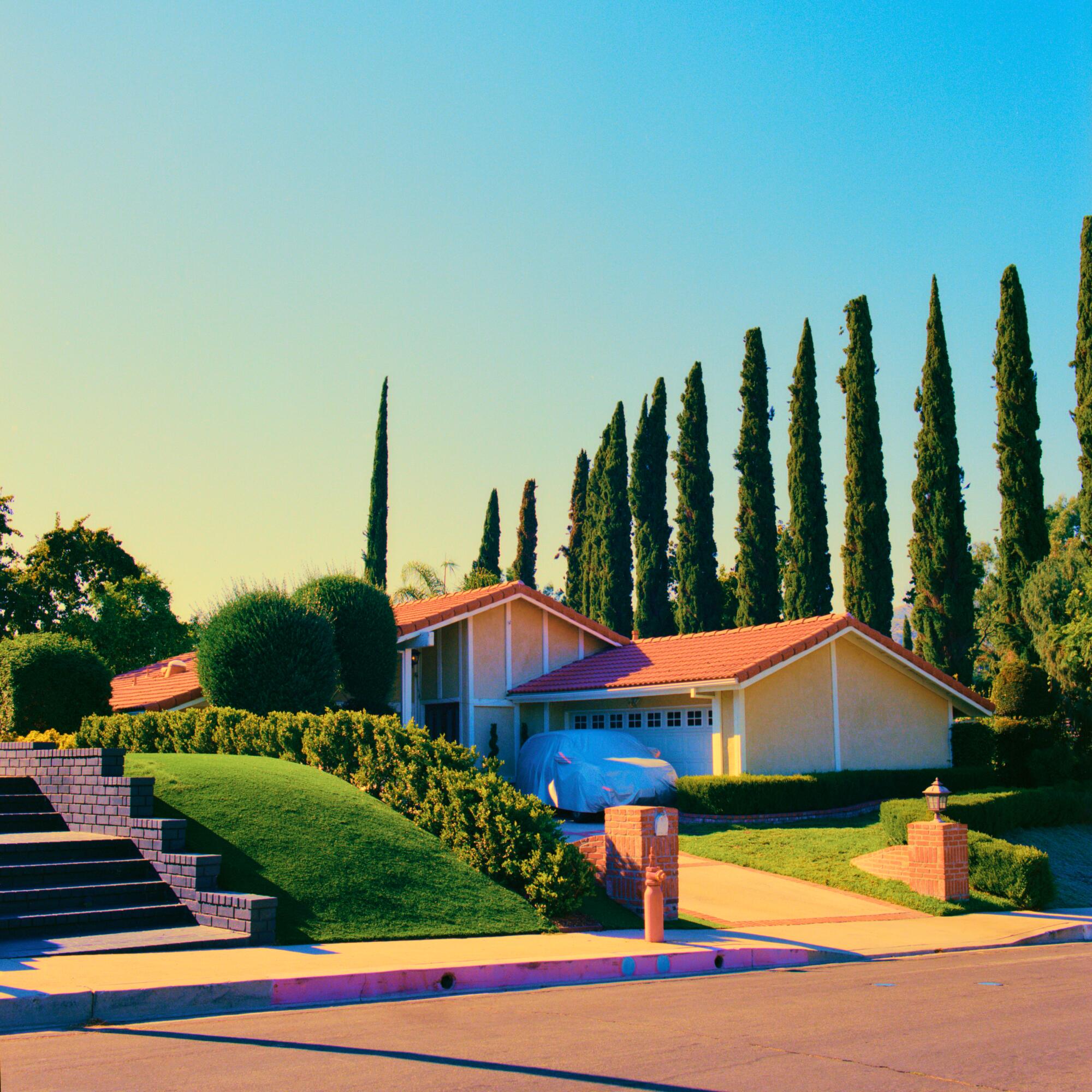 A saturated photo of a house with a red roof and manicured lawn.