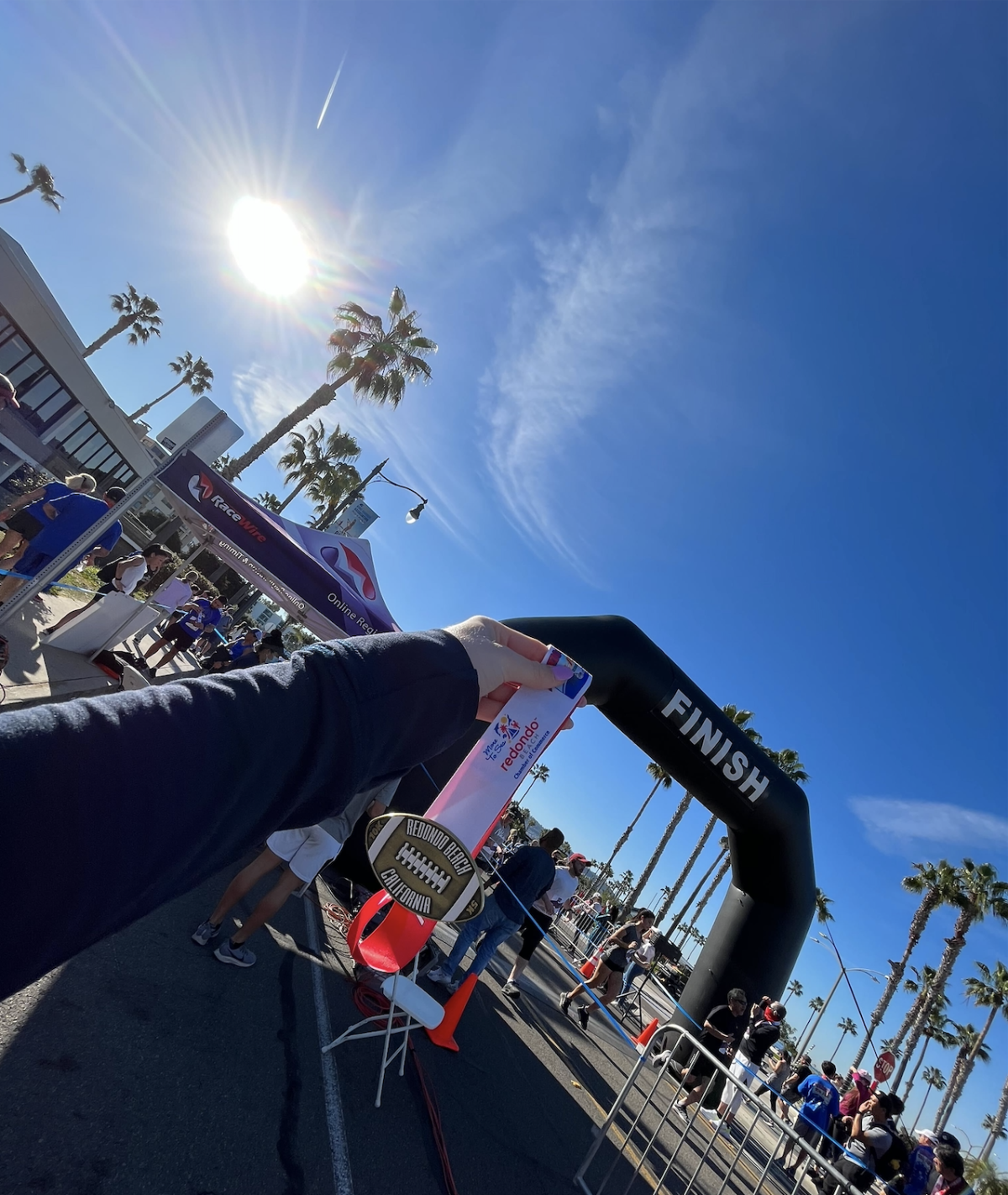A Super Bowl 10k/5k finisher medal held up in front of the finish line at the Redondo Beach Super Bowl Sunday race