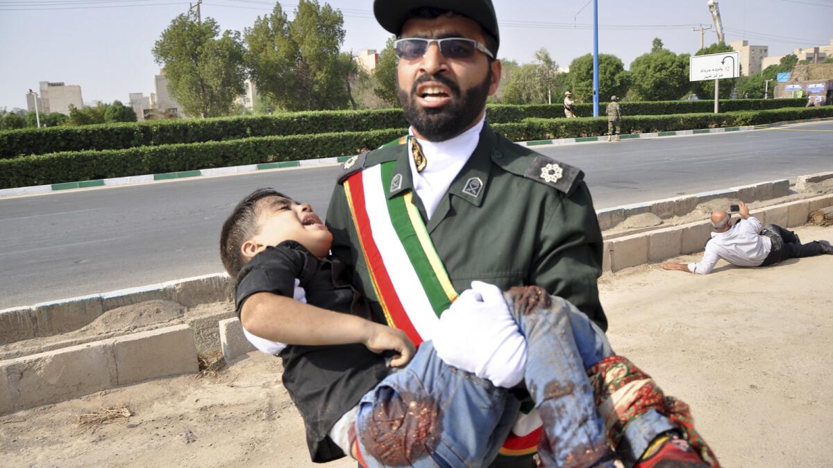 In a photo provided by the Iranian Students' News Agency, a Revolutionary Guard member carries a wounded boy after the shooting at a military parade in Ahvaz, Iran.