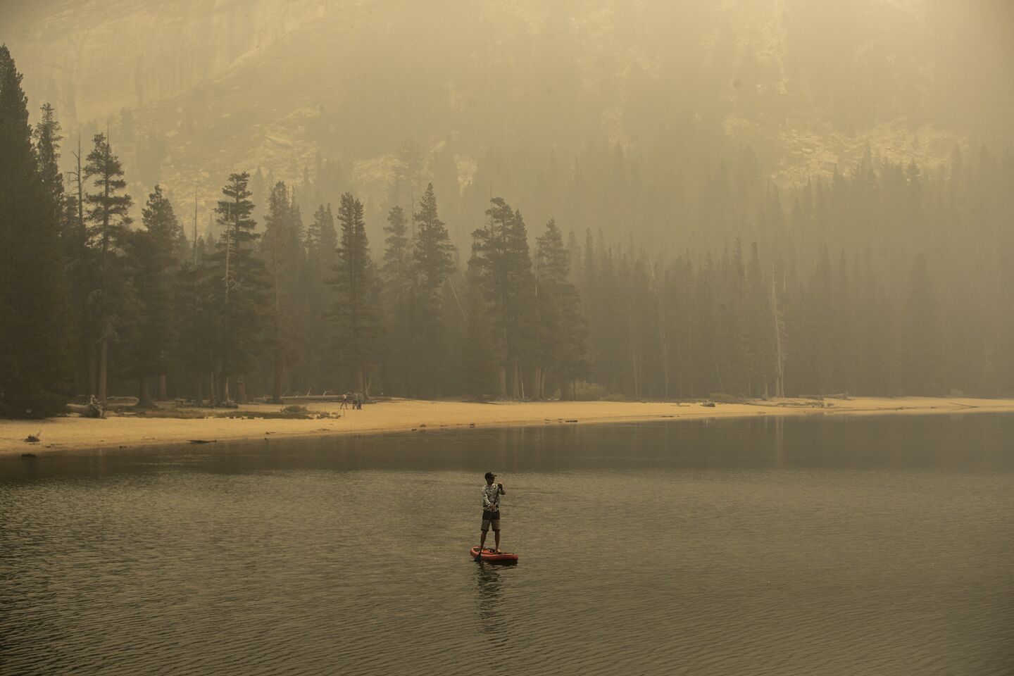 Smoke shrouds forest around Tenaya Lake as a man paddleboards.