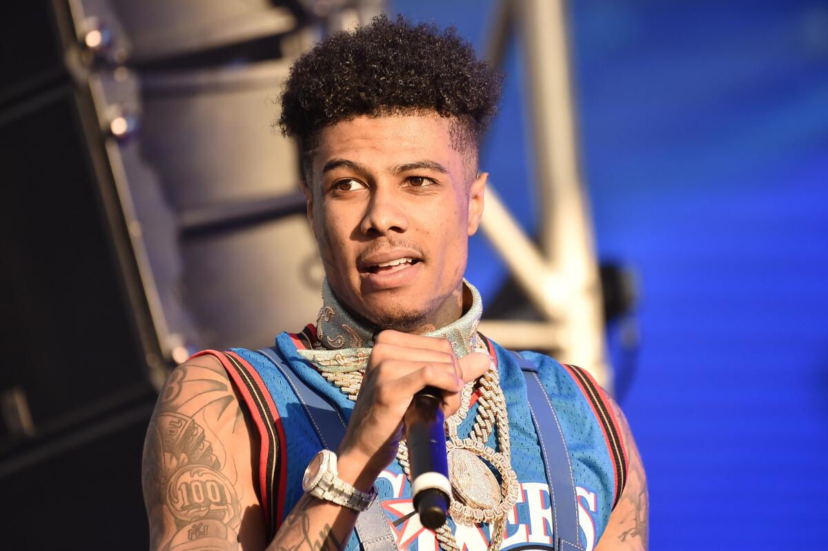 Blueface holds a microphone near his face while wearing a blue basketball jersey onstage