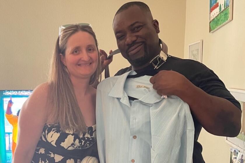 A woman stands next to a man holding a dress shirt on a hanger up to his chest, both smiling.