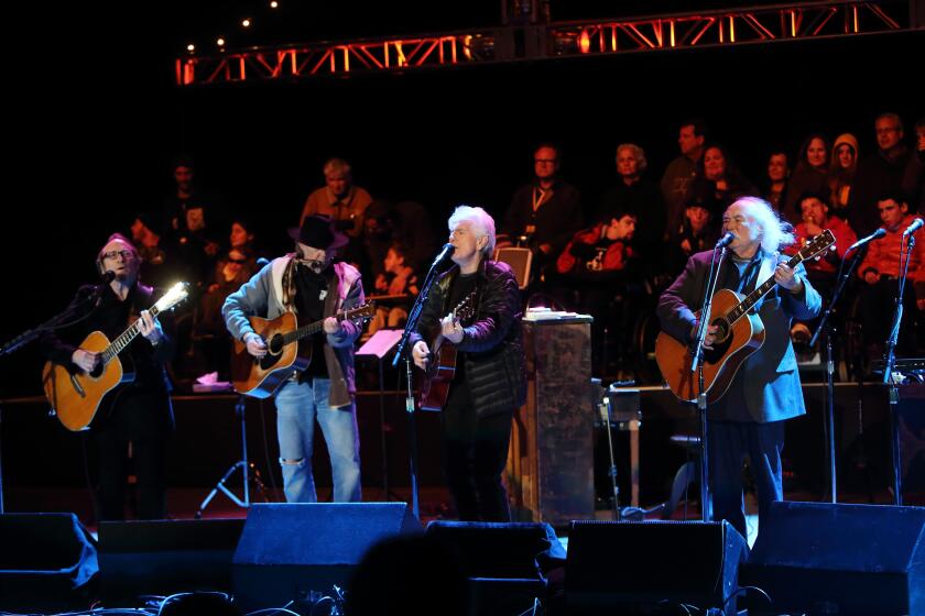 Crosby, Stills, Nash and Young playing guitars and singing into microphones on a stage