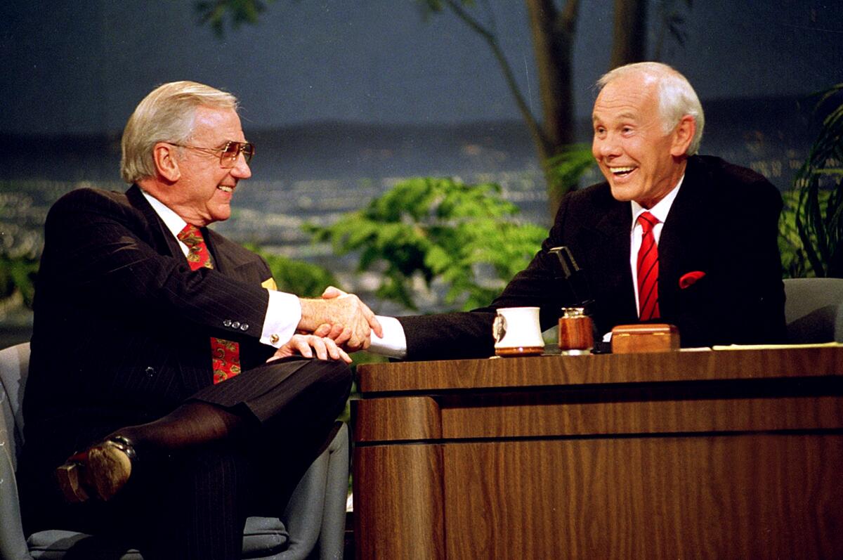 Ed McMahon and Johnny Carson seated, shaking hands.