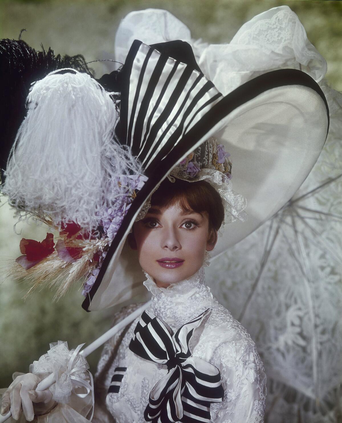 A woman in an 1890s black-and-white dress with a large hat and a lacy parasol.