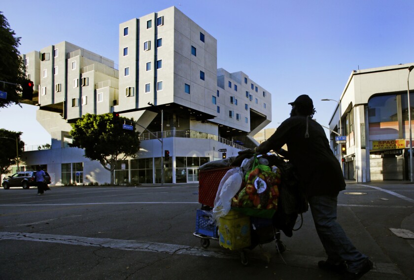 A homeless man crosses the road on skid row with his belongings in a shoping cart.