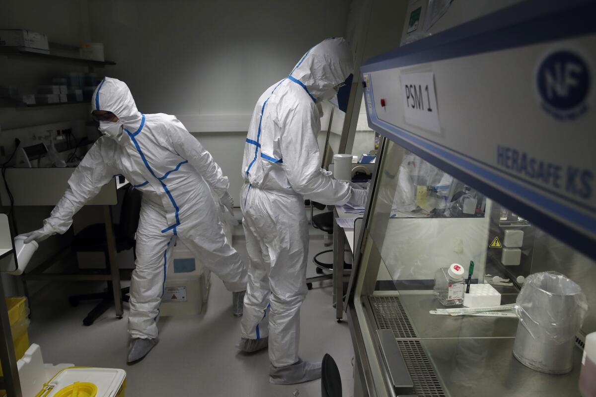 French lab scientists in hazmat gear inserting liquid in test tube manipulate potentially infected patient samples at Pasteur Institute in Paris Thursday.